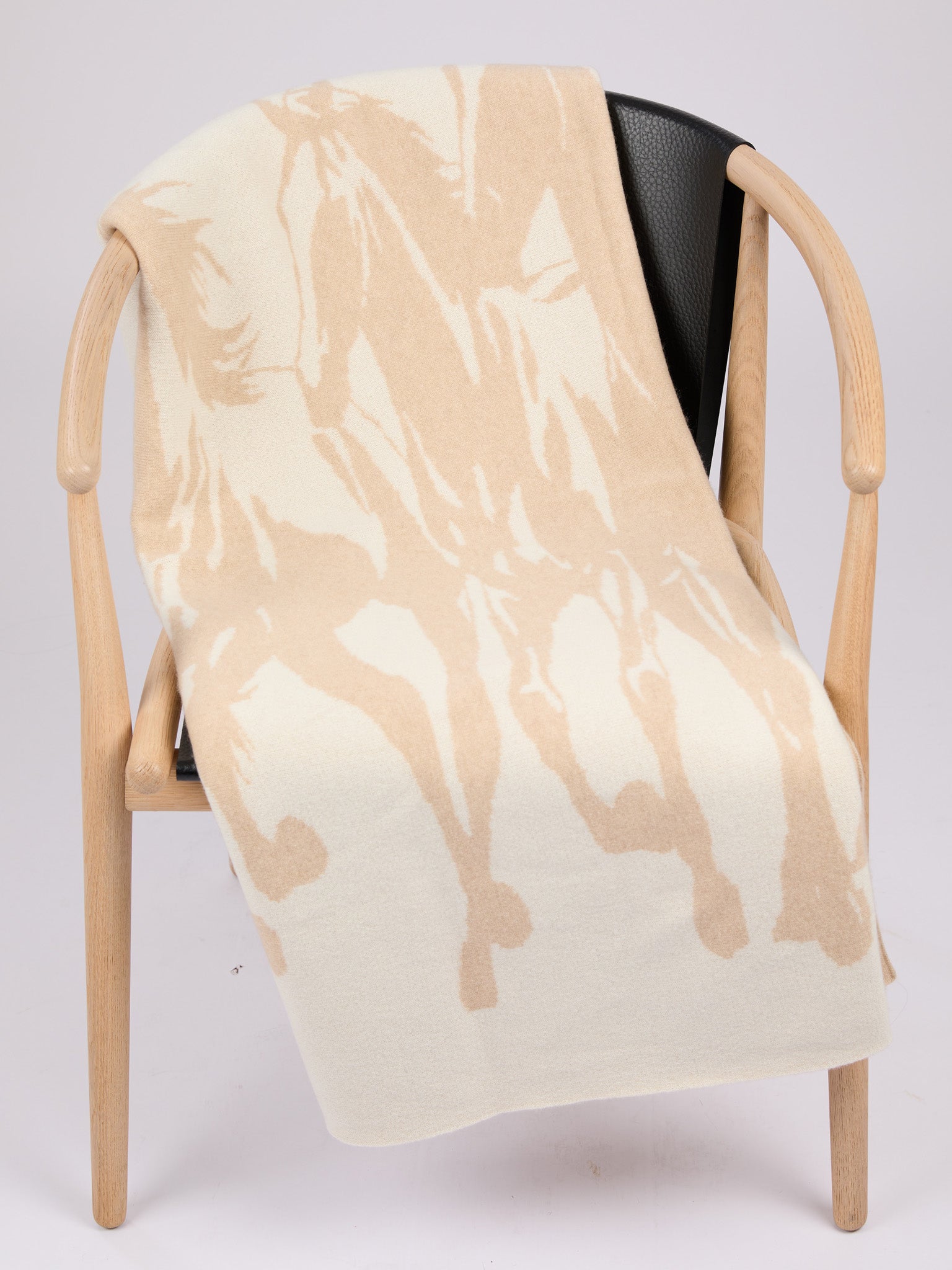 A rectangular cashmere blanket featuring a stylized silhouette of a herd of horses in motion, rendered in a muted oat on a warm pearl background #PEARL/OAT