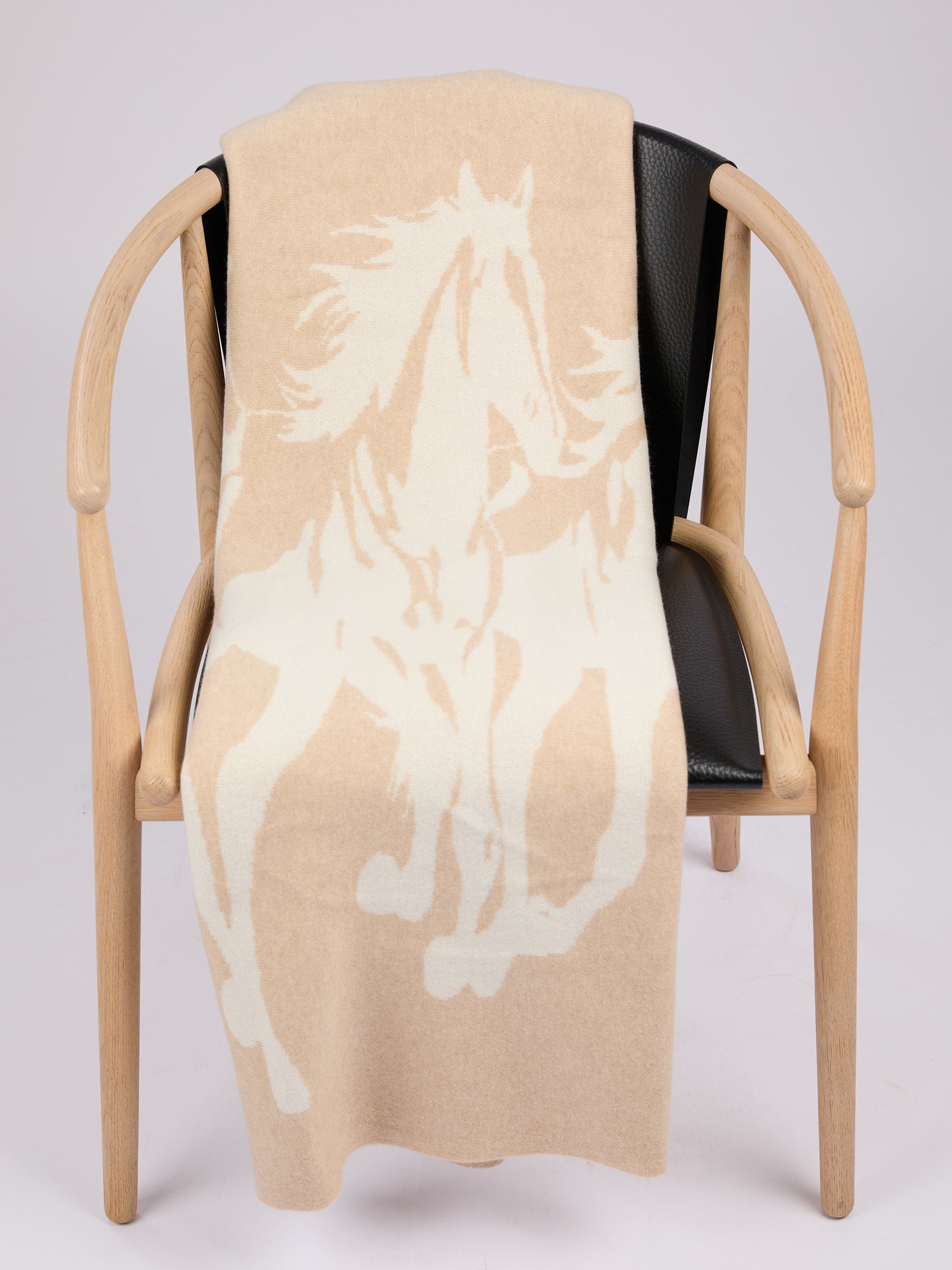 A rectangular cashmere blanket featuring a stylized silhouette of a herd of horses in motion, rendered in a muted oat on a warm pearl background #PEARL/OAT